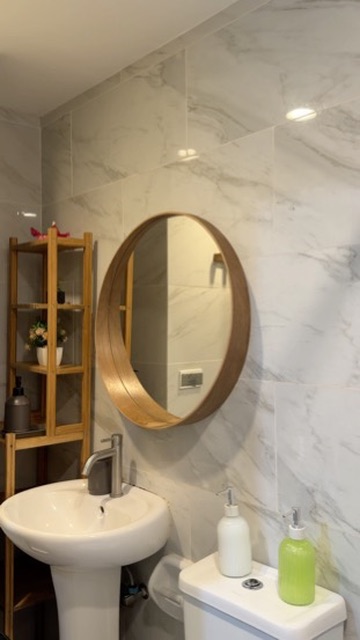 Bathroom vanity at Cityscape Grand Tower with round wooden mirror and marble-patterned walls